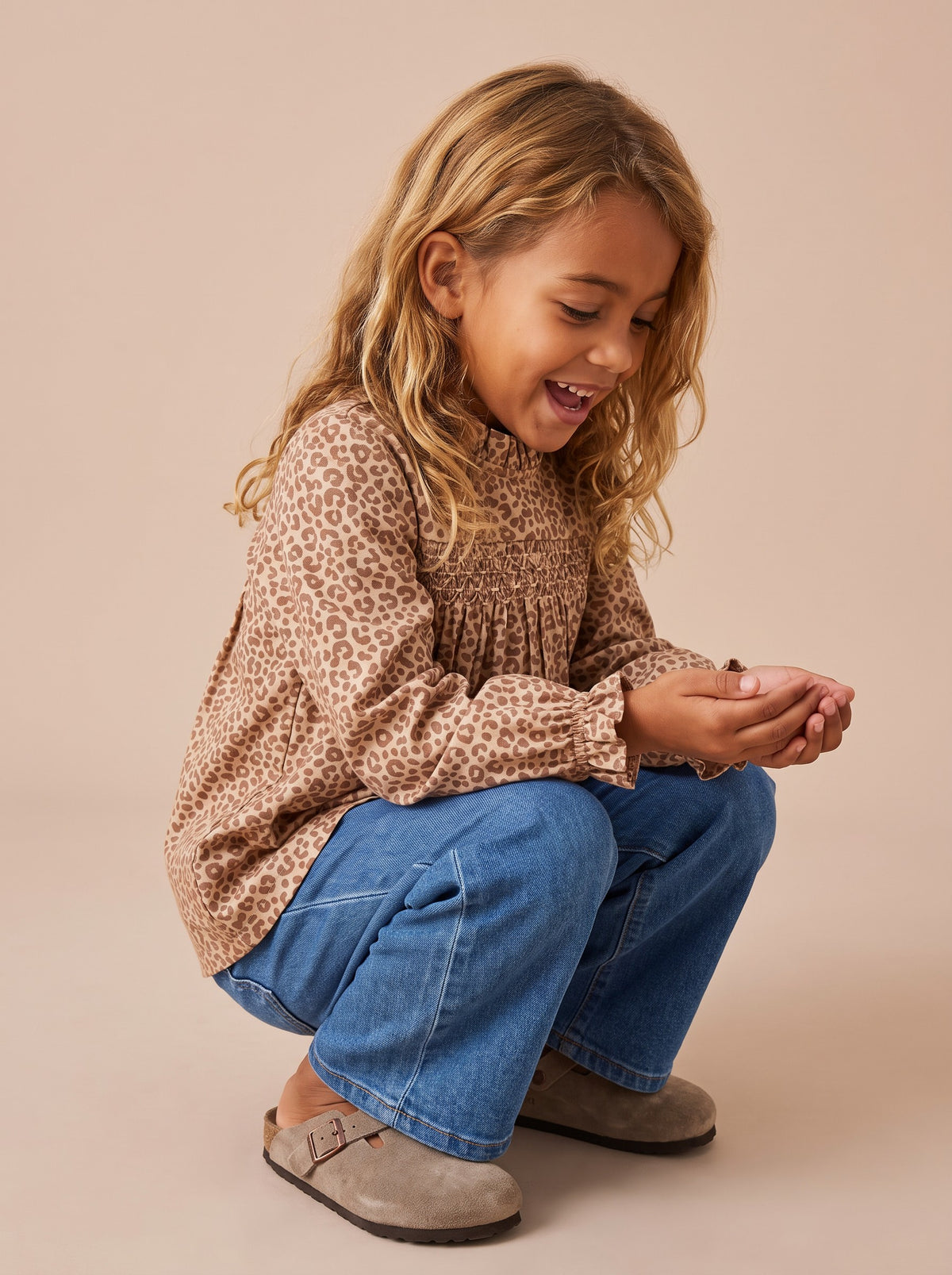 Blouse Mia léopard portée par une petite fille accroupie, jean large et sabots
