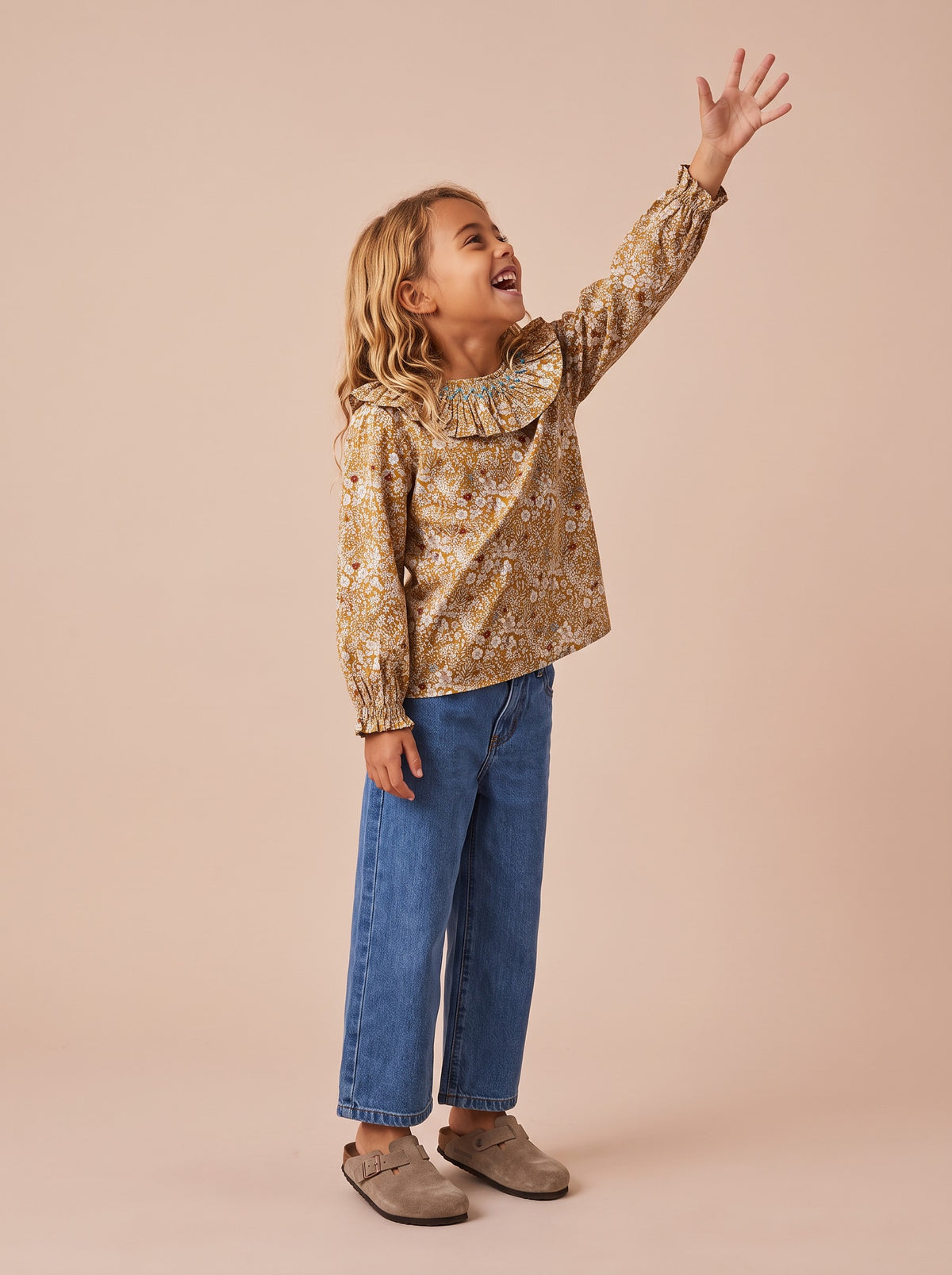 Blouse Rio June beige portée par une petite fille sur la pointe des pieds, jean large