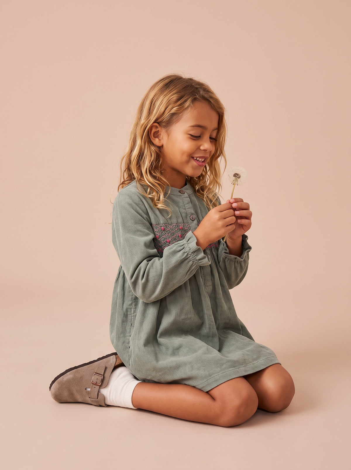 Robe Harper vert sauge portée par une petite fille à genoux soufflant un pissenlit